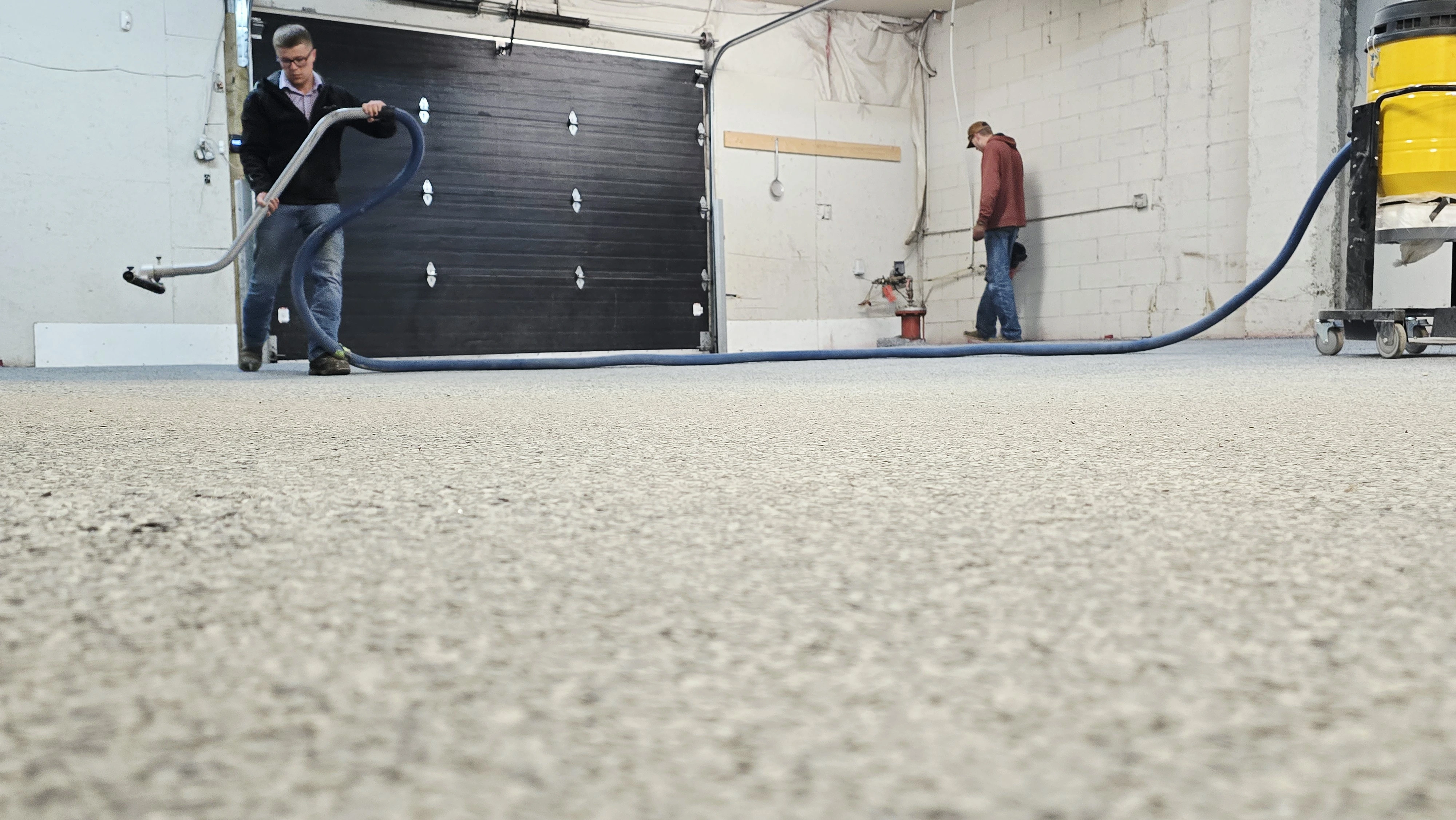 Low angle of a finished flake shop floor with an installer vacuuming and a dust extractor