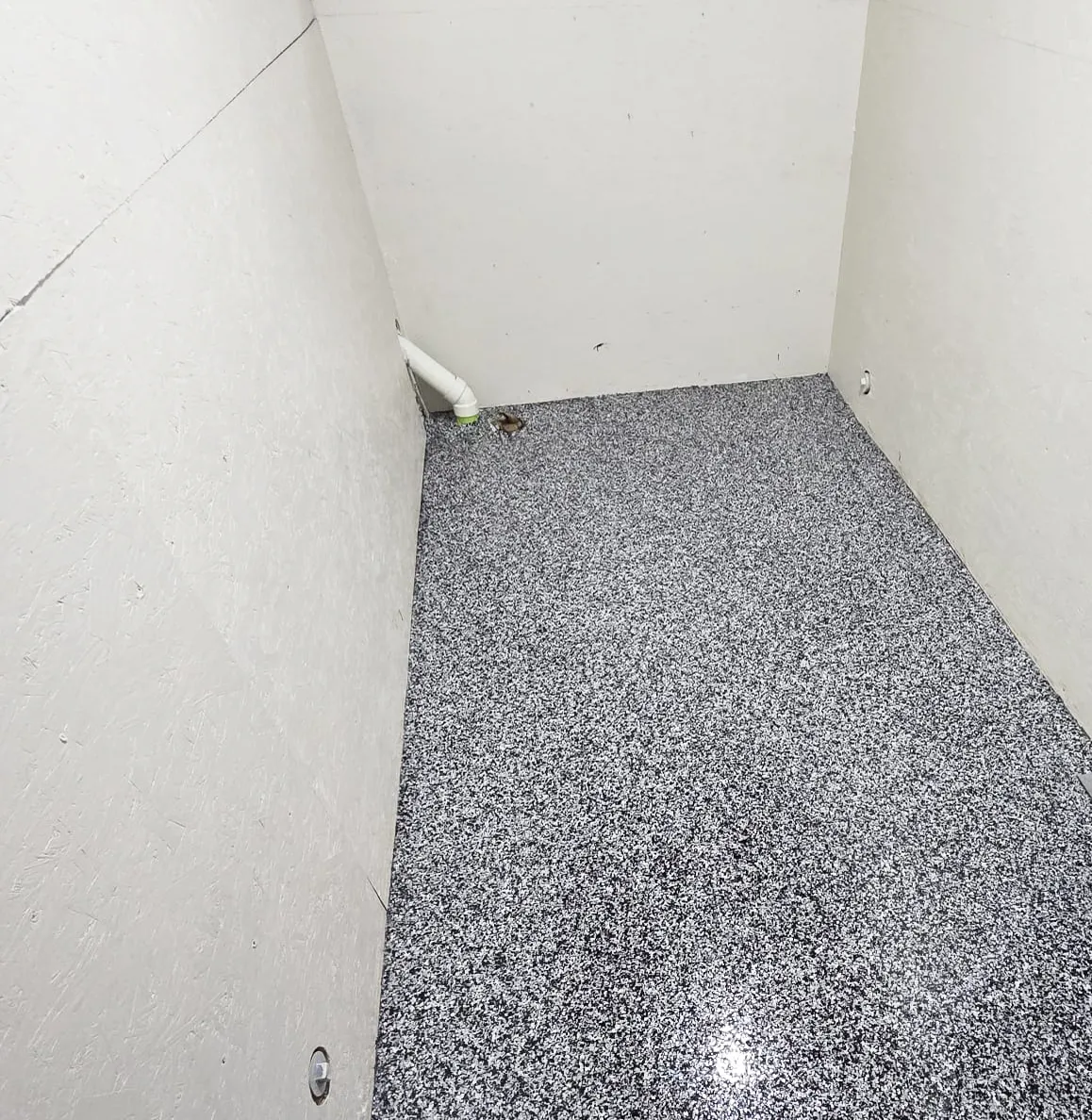 Corner of a basement room finished with a black-and-white flake floor coating against white walls