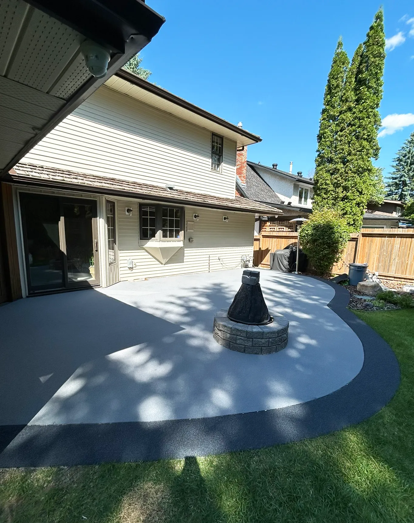 Resurfaced backyard patio in grey rubber pavement with a charcoal border, sliding patio doors and lawn alongside