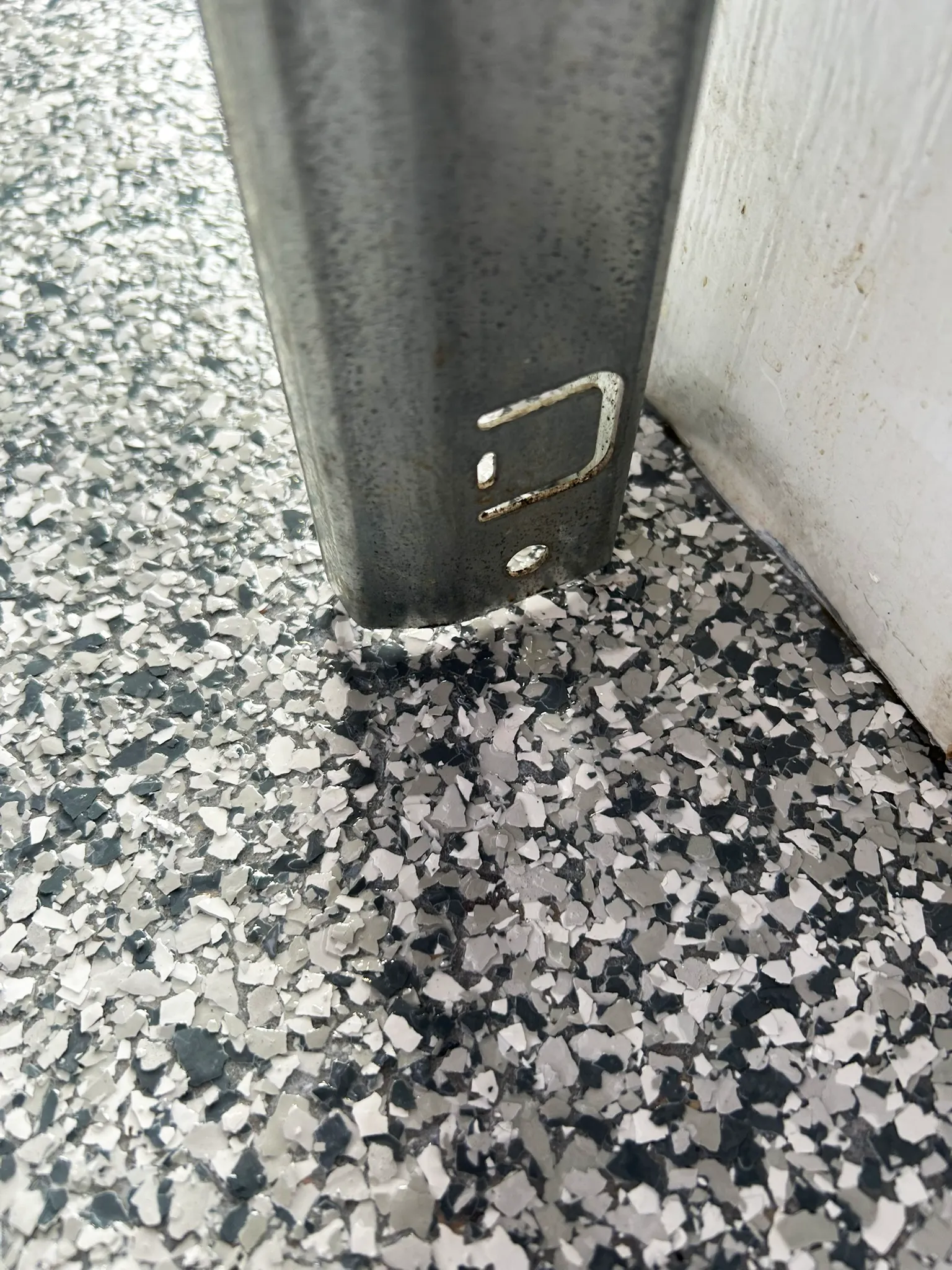 Close-up of white, grey and charcoal coating flakes worked around the base of a galvanized steel post