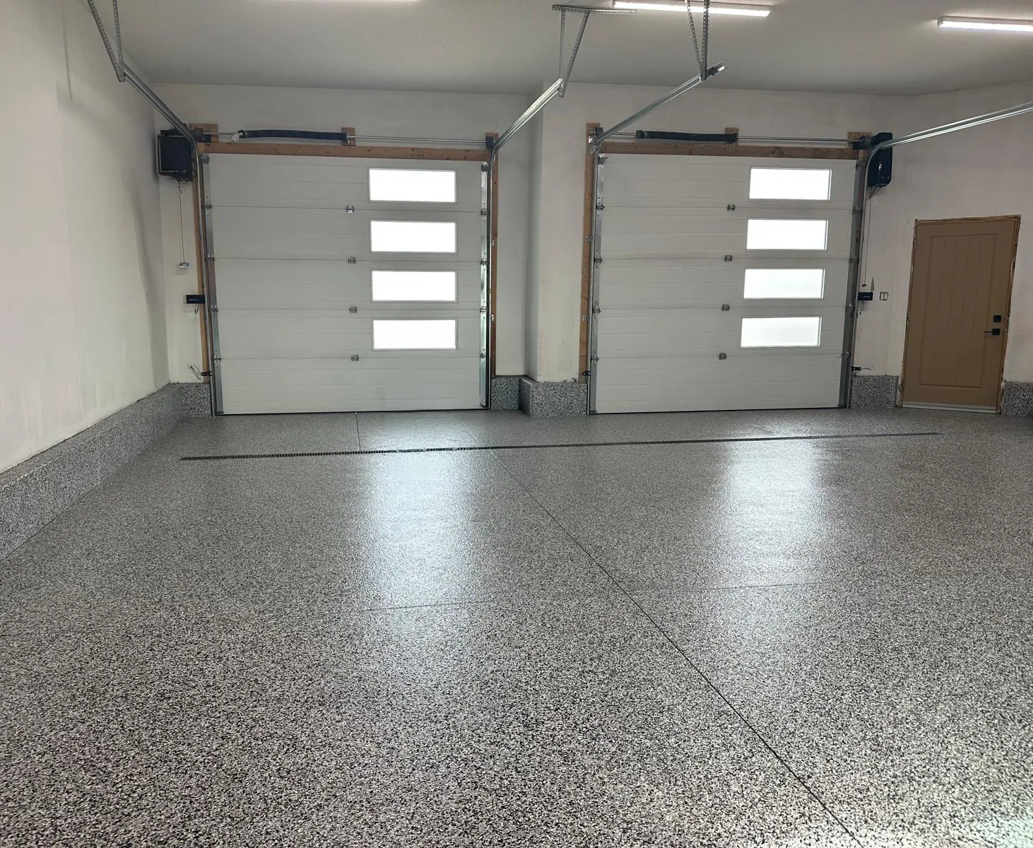 Two-car garage with a grey flake floor coating and two white overhead doors with window panels