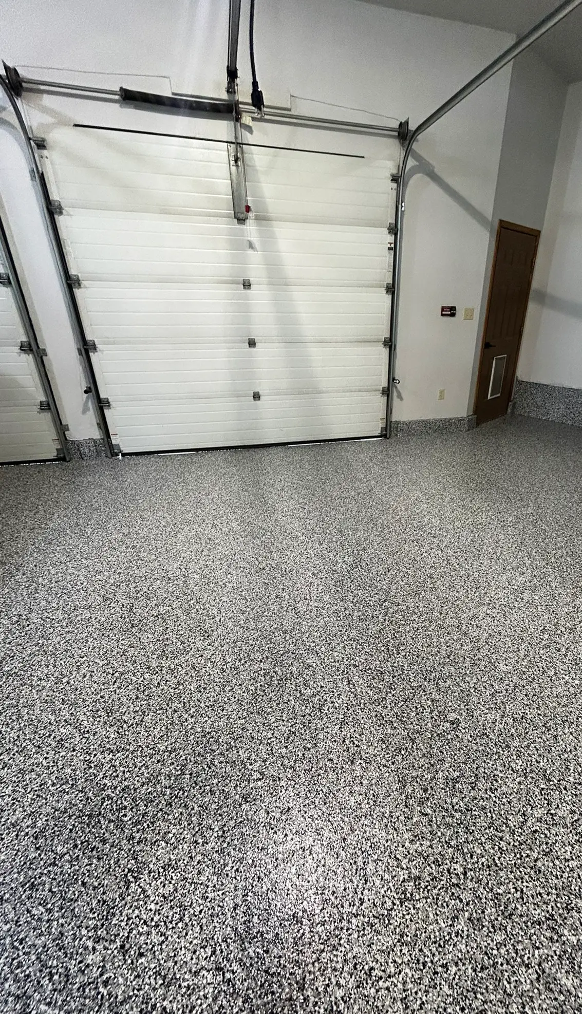 Grey and black decorative flake floor coating in a finished residential garage with a white overhead door